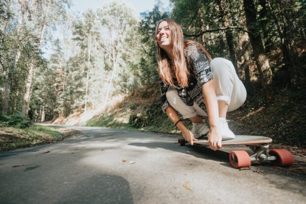 Woman riding a long board on the road in the middle of a moody forest.Practicing outdoors and extrem